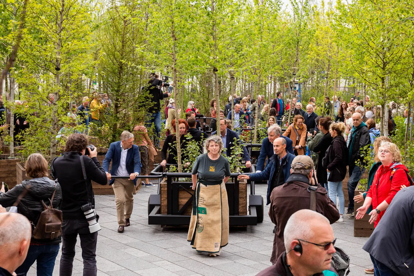 Participatory placemaking event within an urban greening project, featuring mobile tree planters, dense woodland-style planting, and public engagement in the creation of a greener city environment.