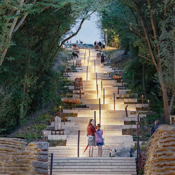 Landscape architecture project featuring a lit stairway integrated into a forested hillside, combining accessibility, public space and ecological design.