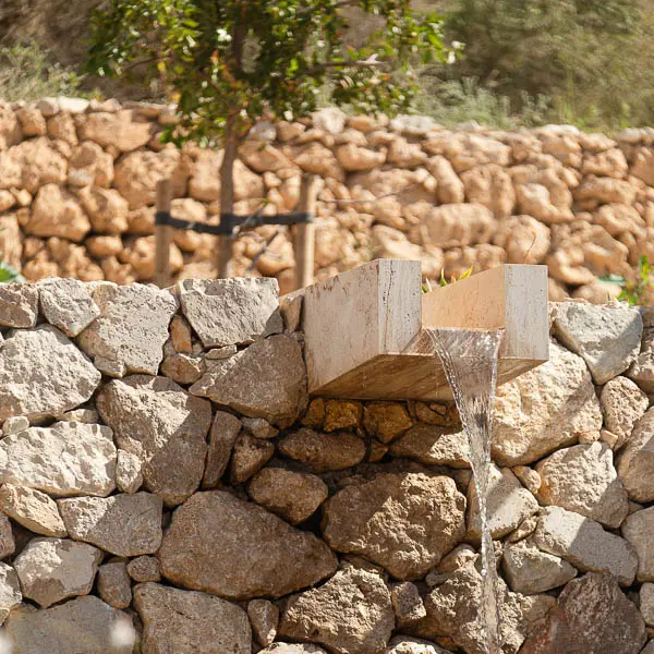 Contemporary water feature built into natural stone terraces, featuring a carved stone spout and flowing water within a restored Mediterranean landscape.